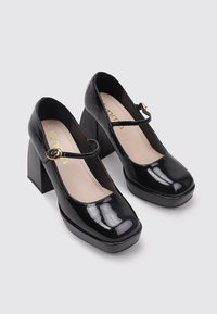 Zapatos de tacón Mary Jane de charol negro con punta cuadrada, tacón cuadrado grueso y una delgada correa de tobillo con un hebilla en tono dorado.