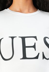 Close-up of a person wearing a white shirt with large black letters "UES" visible across the chest.