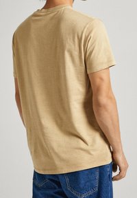 Beige bomullströja med korta ärmar och rund halsringning, med en slät textur och avslappnad passform, bärs ihop med blå denimjeans.