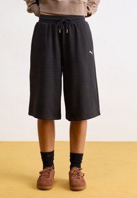 Schwarze Shorts aus weichem Material mit einem elastischen Bund und einem Kordelzug, versehen mit einem kleinen weißen Logo auf der linken Seite.