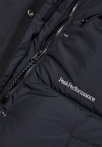 Sort pufferjakke med en blank lynlås, broderet "PeakPerformance" logo i sølv, med en glat, isoleret tekstur og tæt vævning.