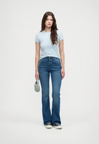 Lichtblauw T-shirt met korte mouwen gecombineerd met flared donkerdenim jeans. De outfit bevat een kleine denim tas en zwart-witte schoenen.