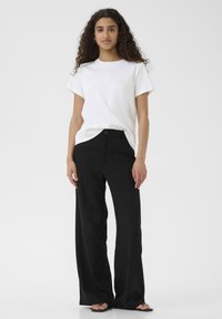 Maglietta bianca a maniche corte abbinata a pantaloni a gamba larga neri a vita alta. Dettagli dei bottoni neri sui pantaloni, texture liscia e vestibilità rilassata.