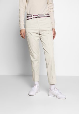 Chinos beige con un design a gamba dritta, caratterizzati da una cintura a righe multicolori e tasche laterali. Indossati con sneakers bianche e calzini alla caviglia.