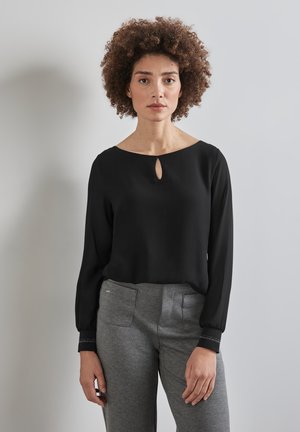 Top nero a maniche lunghe con scollatura a chiave, realizzato in tessuto liscio. Abbinato a pantaloni grigi su misura con tasche frontali.