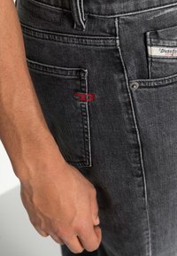 Jeans de denim gris con una ligera textura desgastada, que presentan un pequeño logotipo rojo bordado en el bolsillo lateral y acentos de hardware plateado.