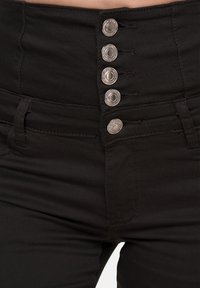 Jeans neri a vita alta con cinque bottoni decorativi d'argento, caratterizzati da una texture liscia e sottili dettagli di cucitura.