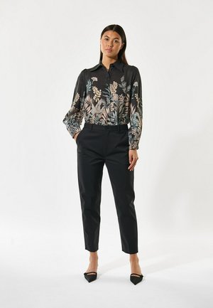 Black blouse with floral pattern, collared design, and elasticized cuffs, paired with tailored black trousers and black pointed-toe shoes.