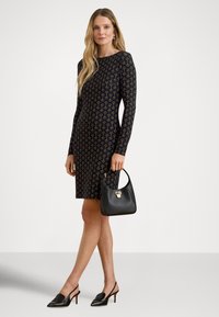 Sort kjole med lange ermer med et gyllent geometrisk mønster. Brukt med en liten svart håndveske og spisse svarte hæler.