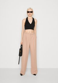 Svart halterneck crop top, beige høye bukser med knappdetalj, kombinert med svarte solbriller og en liten svart håndveske.