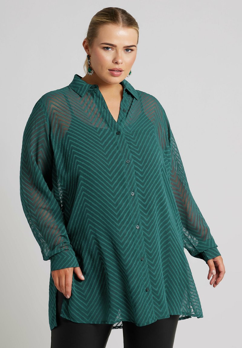 Zielona przezroczysta koszula na guziki z wzorem w zygzak, długimi rękawami i kołnierzykiem. Charakteryzuje się luźnym krojem oraz bocznymi rozcięciami u dołu.