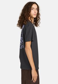 Schwarzes Baumwoll-T-Shirt mit kurzen Ärmeln, das auf der linken Seite ein lila grafisches Muster aufweist. Klassisches Rundhalsausschnitt-Design.
