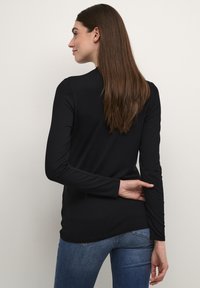 Langärmliges schwarz Oberteil aus einem weichen, elastischen Stoff, mit abgerundetem Saum und seitlichen Schlitzen, kombiniert mit blauen Jeans.