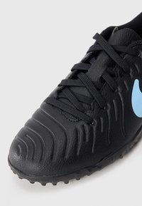 Baskets de sport noires à texture, avec des lacets noirs et le logo Nike bleu sur le côté, sur un fond blanc uni.