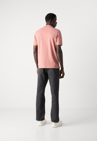 Polo rose à manches courtes avec une texture douce, assorti à un jean en denim noir et des baskets blanches, vu de dos.
