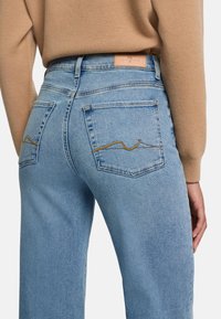 Hellblaue Jeans mit hoher Taille, ausgestattet mit einem Lederpatch auf der Rückseite und Zickzacknähten an den Taschen.