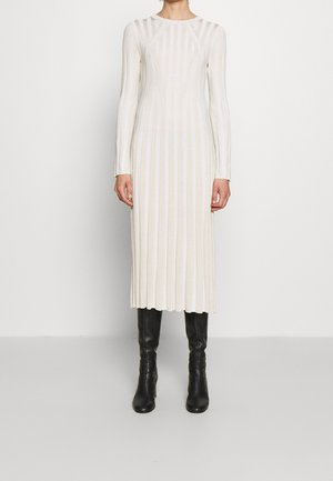 Kobieta w długiej kremowej sukience z dzianiny prążkowanej z długimi rękawami, połączonej z czarnymi skórzanymi kozakami do kolan.