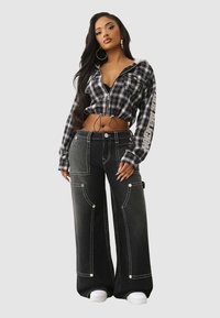 Czarno-biały kraciasty krótki hoodie z zamkiem i detalem w postaci sznureczka, połączony z szerokimi czarnymi spodniami z białymi przeszyciami i kieszeniami.