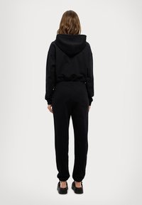 Schwarzer Hoodie und passende Jogginghose aus weichem Material, mit einer Fronttasche, elastischen Bündchen und einem lässigen Schnitt.