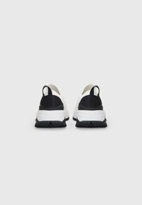 Zapatillas deportivas en blanco y negro con parte superior texturizada, suela acolchada y pestañas en el talón prominentes para facilitarlas al ponérselas. Suela de goma para mayor tracción.