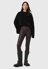 Czarny, puszysty, oversize sweter, dopasowane brązowe legginsy z sztucznej skóry i czarne kozaki za kolano z akcentami w postaci klamer. Prosty i teksturowany design.