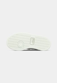 Suola nera della sneaker con una parte inferiore in gomma bianca testurizzata. Presenta un elemento di design circolare e il logo del marchio vicino al tallone.