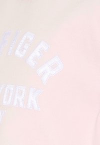 Lichtroze sweatshirt met geborduurde witte tekst "TIGER NEW YORK" in een vette lettertype. Zachte stof en een casual pasvorm.