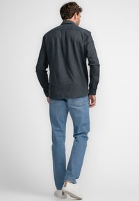 Donkergrijs, knoopshirt gemaakt van textiel, gecombineerd met lichtblauwe spijkerbroek en witte sneakers, wat een casual stijl uitstraalt.