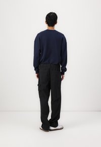 Sweatshirt azul-marinho de mangas longas, combinado com calças cargo pretas com bolsos laterais. O modelo está de costas contra um fundo simples.