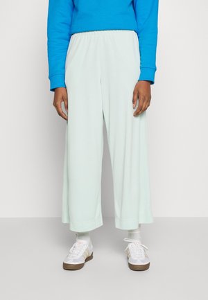 Helle mintgrüne, weite Hose mit einem elastischen Bund, aus weichem Stoff, kombiniert mit weißen Sneakers und einem blauen Sweatshirt.