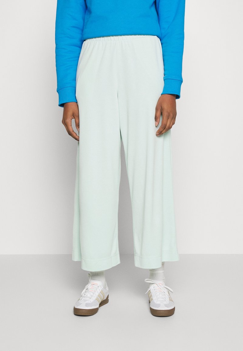 Helle mintgrüne, weite Hose mit einem elastischen Bund, aus weichem Stoff, kombiniert mit weißen Sneakers und einem blauen Sweatshirt.