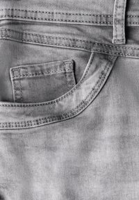 Close-up of grey denim jeans pocket with visible stitching and a small coin pocket inside the main pocket.