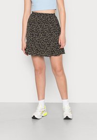 Saia preta floral com cintura franzida, apresentando pequenas flores roxas e amarelas. Usada com meias brancas e ténis.