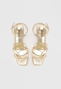 Sandale aurii cu toc înalt, vârf pătrat, barete decorative metalice și o parte frontală texturată sclipitoare. Căptușeală interioară netedă și logo-ul brandului vizibil.