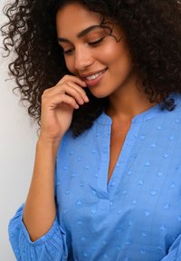 Svetlomodrá blúzka z textúrovaného materiálu, s výstrihom na zapínanie, zdobená nariasenými rukávmi a vystúpenými vzormi v tvare srdca.