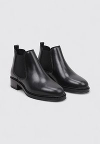 Botas Chelsea de cuero negro con paneles laterales elásticos, punta redondeada y un tacón bajo apilado. Textura suave y detalles de costura mínimos.