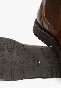 Bruine leren enkellaars met een gladde afwerking en elastische zijkanten. De rubberen zool met profiel heeft een logo en detail van de Italiaanse vlag.