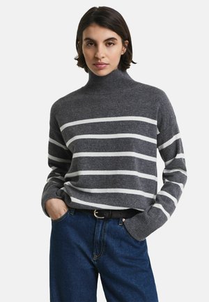 Grijs gestreepte trui met een hoge halslijn en lange mouwen, voorzien van witte horizontale strepen en een zachte brei-structuur. Gecombineerd met blauwe jeans.