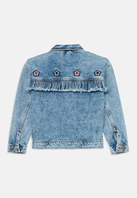 Lys blå denimjakke med frynset bakhem. Har tre broderte stjerner i rødt, hvitt og svart over skulderen.