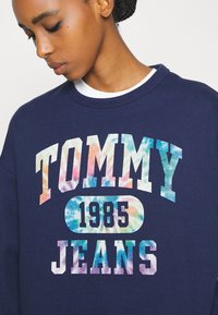 Námornícky sveter s nápisom "TOMMY" v multikolórovom gradientovom prevedení, s nápisom "JEANS" a "1985" v tučnom písmene. Vyrobený z bavlny, vo voľnom strihu, s okrúhlym výstrihom.