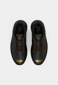 Para czarnych sneakersów Nike Air Jordan z brązowymi sznurówkami i przeszyciami, złotymi płytkami na palcach, widzianych z góry na białym tle.