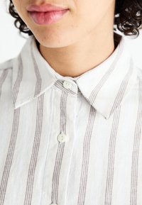 Chemise à rayures en tissu léger, avec des rayures étroites marron et blanches, col pointu et boutons blancs.