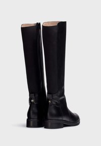 Bottes noires montantes en cuir lisse, avec une fermeture éclair à l'arrière et des accents subtils en métal doré sur le talon.