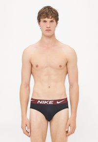 Black brief with a maroon Nike-branded waistband featuring white logo accents. Soft, stretchy material designed for comfort and fit.