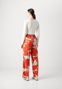 Long-sleeve cream top paired with wide-leg red and white floral-patterned pants, featuring an elastic waistband and smooth fabric texture.