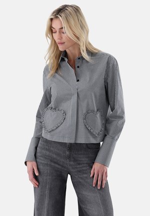 Black and white checked cropped shirt with heart-shaped pockets, buttoned front, and collar; paired with gray wide-leg jeans.