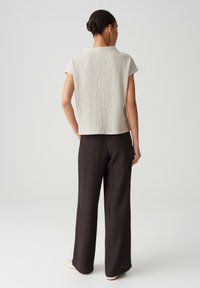 Beige textured short-sleeve top with a high neckline paired with dark wide-leg trousers. Flat shoes complete the outfit.