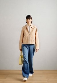 Ανοιχτό μπεζ κοντό μπουφάν με γιακά, συνδυασμένο με φαρδιά μπλε τζιν. Κάτω από αυτό υπάρχει λευκό πουκάμισο και κίτρινη τσάντα. Φόντο από ξύλινο δάπεδο.