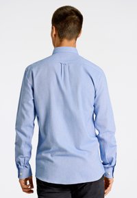 Vaaleansininen pitkähihainen paita, jossa on säädelty kaulus, takahameen yksityiskohta ja napitettu hihansuu, valmistettu sileästä, kevyestä kankaasta.