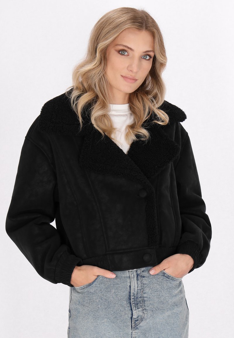 Schwarze, kurze Jacke mit plüschigem Schafsfellkragen, Knopfverschlüssen und elastischen Bündchen, kombiniert mit ausgewaschenen blauen Jeans.